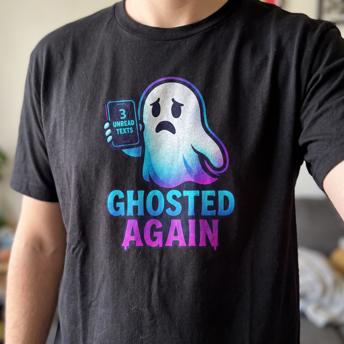 Person wearing the black Ghosted Again graphic tee — cartoon ghost holding a phone with 3 unread texts, GHOSTED AGAIN in a blue-purple gradient