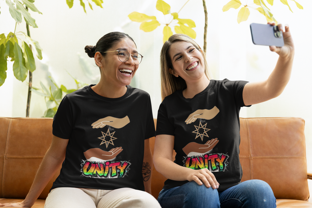 Unity positive message graphic t-shirt worn by two happy women taking selfie while sitting couch