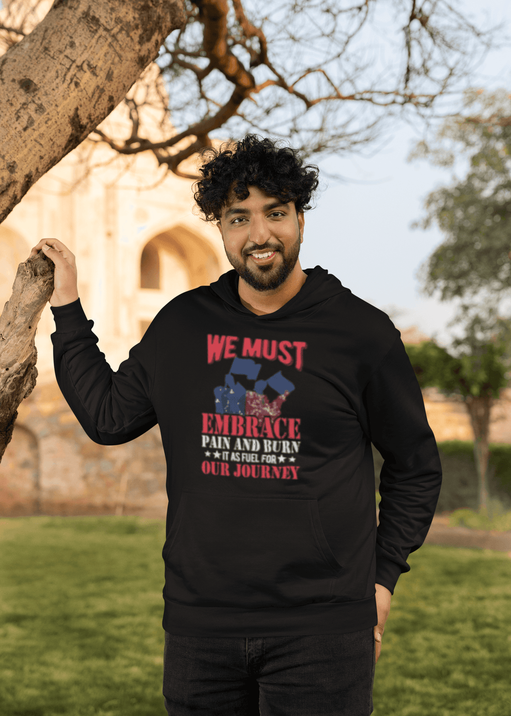 Embrace Pain hoodie worn by smiling bearded man posing near tree